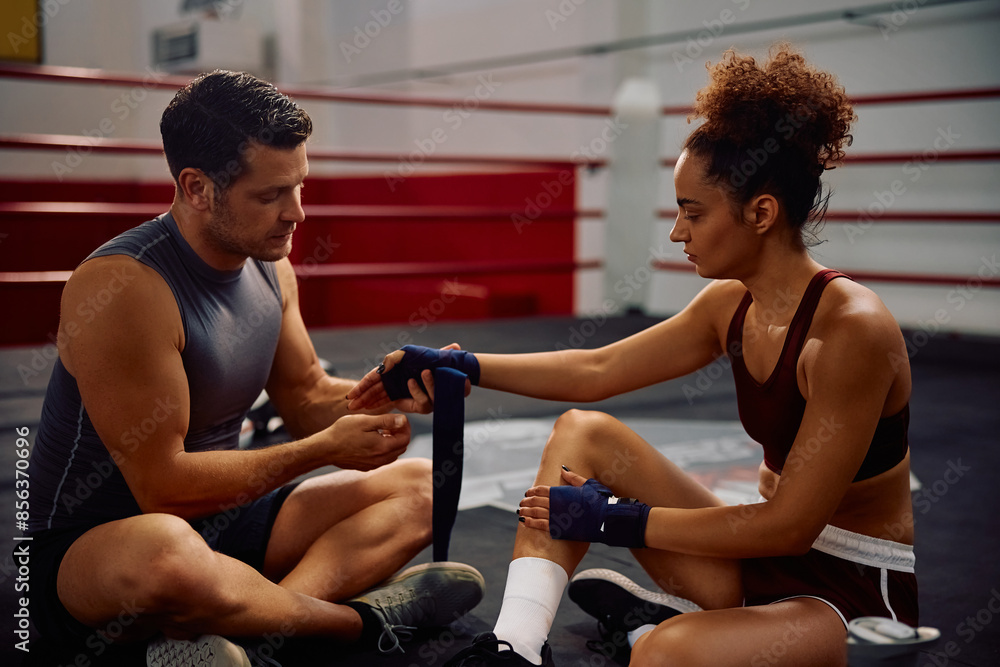 Boxing instructor wrapping sportswoman's hands with bandage before training in health club. Boxing instructor wrapping sportswoman's hands with bandage before training in health club.
