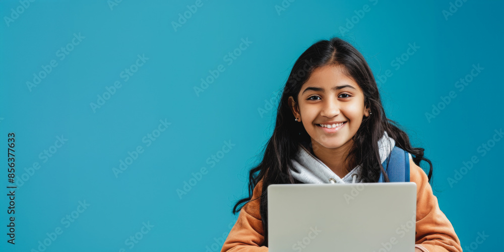 Smiling indian teen girl uses laptop for online study in front of blue background Smiling indian teen girl uses laptop for online study in front of blue background