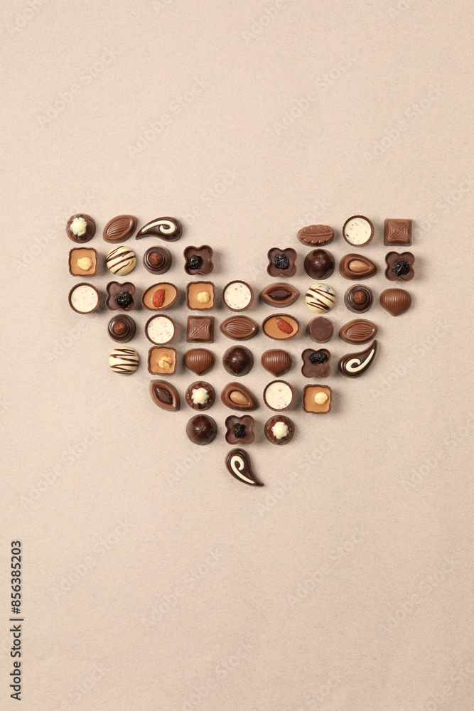 Heart made with delicious chocolate candies on beige background, top view Heart made with delicious chocolate candies on beige background, top view