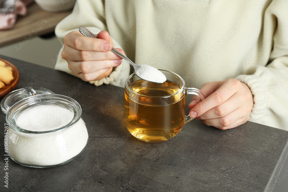 Woman adding sugar into aromatic tea at grey table, closeup Woman adding sugar into aromatic tea at grey table, closeup