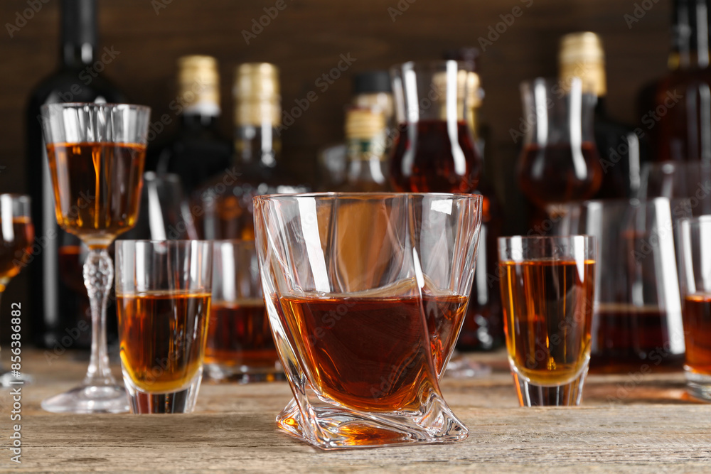 Different delicious liqueurs in glasses and bottles on wooden table Different delicious liqueurs in glasses and bottles on wooden table
