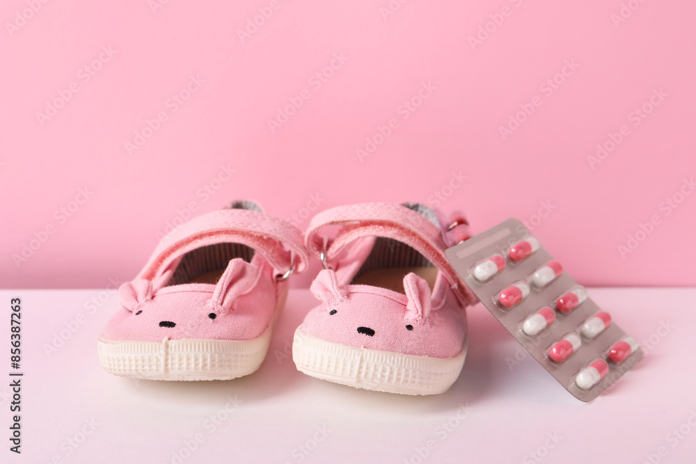 Cute baby shoes and pills on color background Cute baby shoes and pills on color background