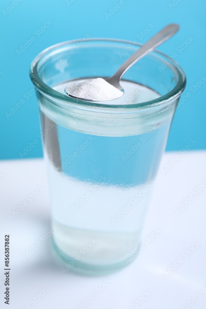 Glass of water and spoon with baking soda on color background, closeup Glass of water and spoon with baking soda on color background, closeup
