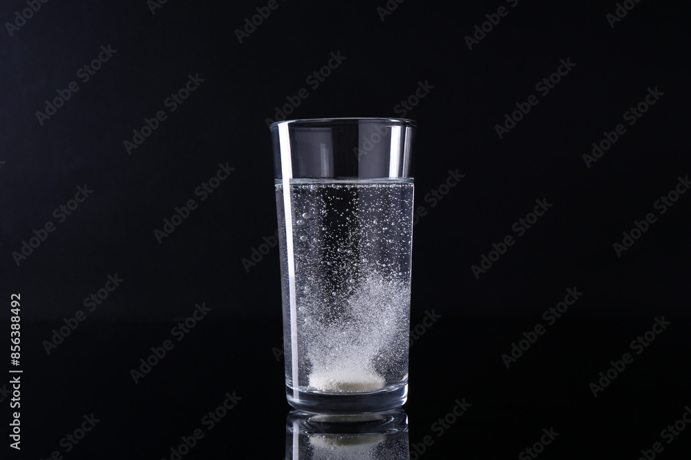 Effervescent pill dissolving in glass of water on black background Effervescent pill dissolving in glass of water on black background