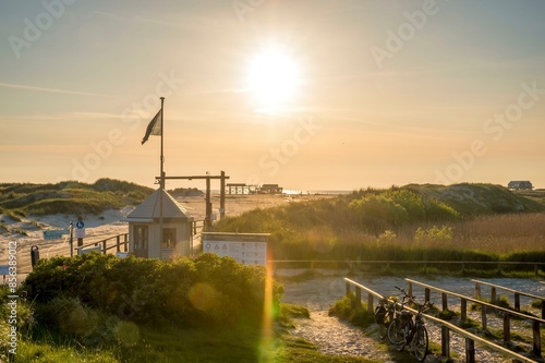 Beach access in the dunes with map house and bicycle stands backlit by the evening sun, St. Peter Ording, Schleswig Holstein, Germany, Europe photo