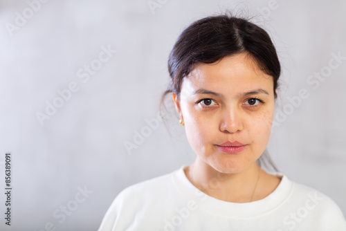 Tableau sur toile Closeup portrait of focused serious young brunette with hair tied back in bun, looking at camera confidently