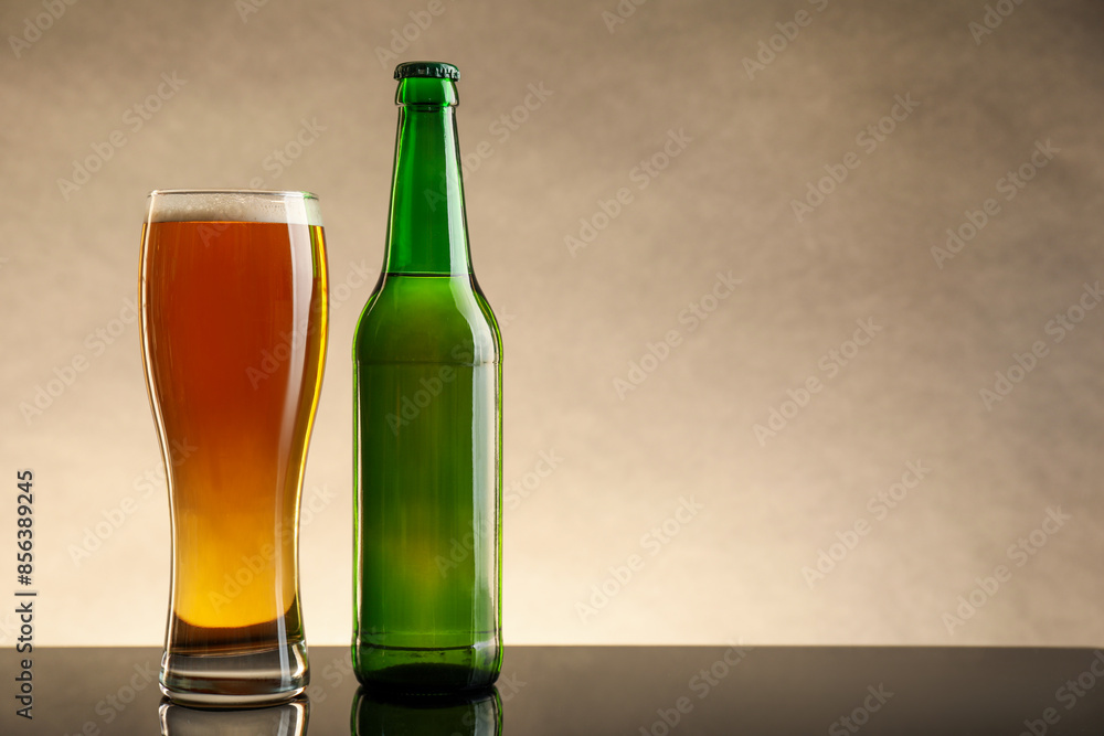 Bottle and glass of beer on table against beige background. Space for text Bottle and glass of beer on table against beige background. Space for text