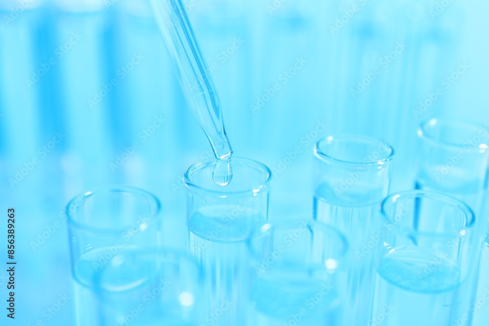 Dripping liquid from pipette into test tube on light blue background, closeup Dripping liquid from pipette into test tube on light blue background, closeup