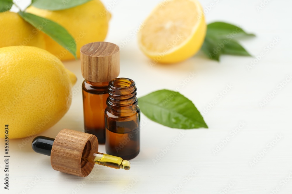 Essential oils in bottles, dropper, lemons and green leaves on white table Essential oils in bottles, dropper, lemons and green leaves on white table