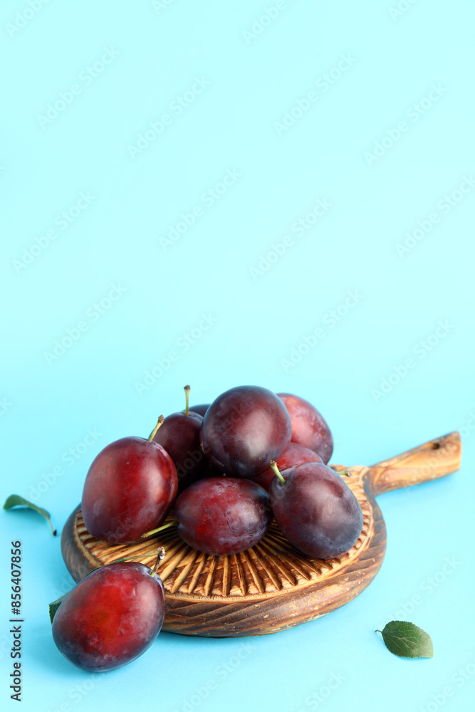 Obraz premium Wooden board with fresh ripe plums on blue background
