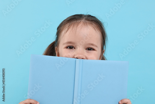 Cute little girl with open book on light blue background