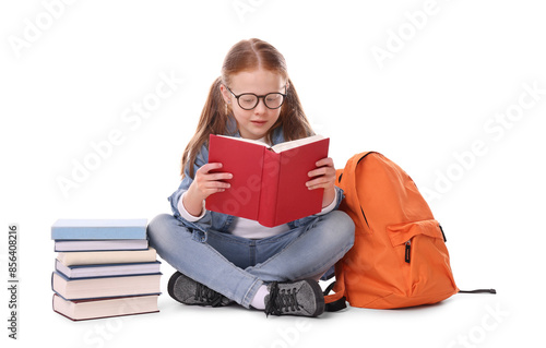 Cute little girl reading book near backpack on white background