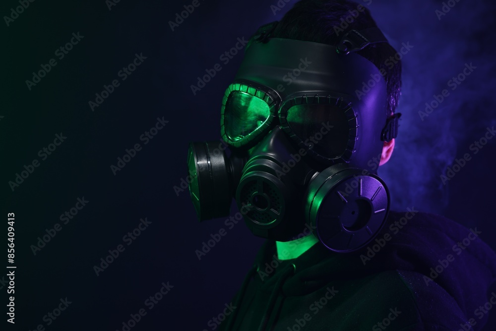 Man wearing gas mask in color lights and smoke on black background. Space for text Man wearing gas mask in color lights and smoke on black background. Space for text