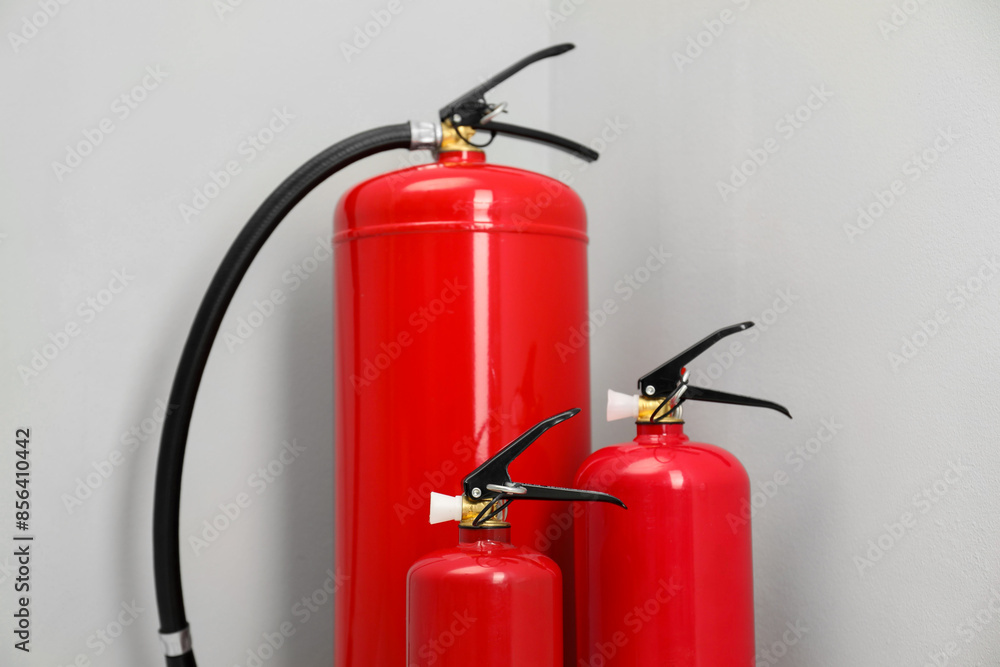 Three fire extinguishers near light grey wall Three fire extinguishers near light grey wall