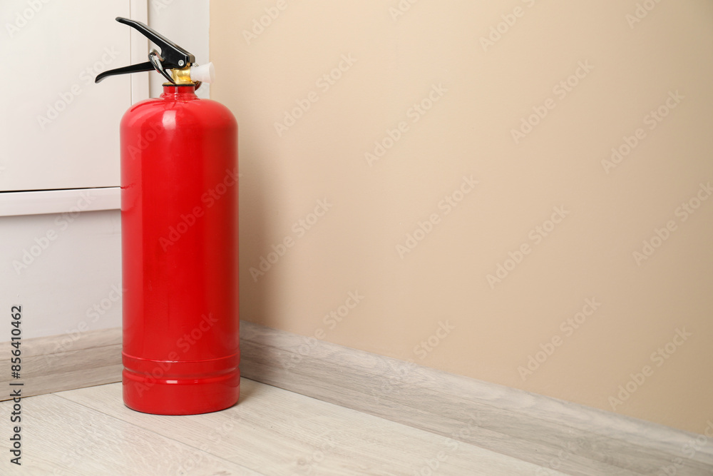 Fire extinguisher on floor near beige wall indoors, space for text Fire extinguisher on floor near beige wall indoors, space for text