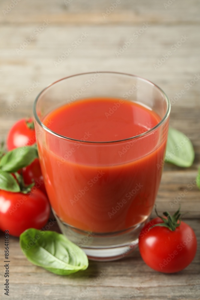 Tasty tomato juice in glass, basil leaves and fresh vegetables on wooden table, closeup Tasty tomato juice in glass, basil leaves and fresh vegetables on wooden table, closeup
