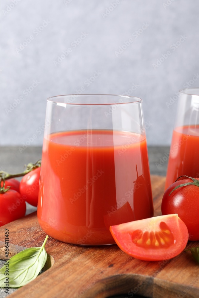 Tasty tomato juice in glass, basil and fresh vegetables on table Tasty tomato juice in glass, basil and fresh vegetables on table