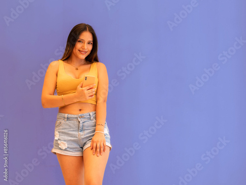 Primer plano de una mujer joven en un traje de verano en un top amarillo con celular.Mujer feliz posando aislada sobre fondo de pared gris hablando por teléfono móvil feliz, sonrisa,