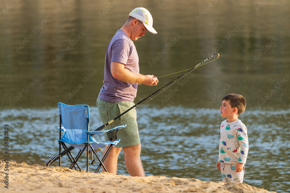 A man and a young boy fishing together on a river bank A man and a young boy fishing together on a river bank