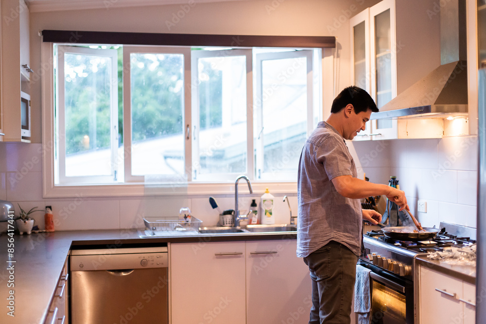 Man standing in the kitchen cooking food in a stovetop pan Man standing in the kitchen cooking food in a stovetop pan
