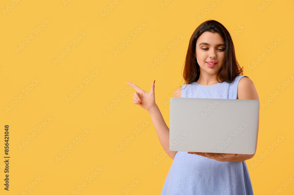 Young woman with laptop pointing at something on yellow background. Online dating concept Young woman with laptop pointing at something on yellow background. Online dating concept