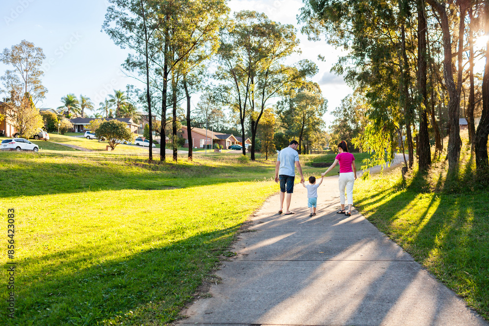 Family of three with toddler on suburban walk in afternoon light on footpath Family of three with toddler on suburban walk in afternoon light on footpath