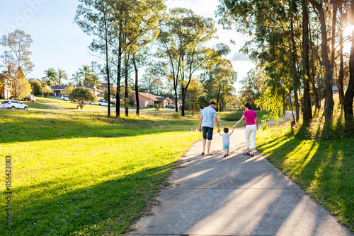 Family of three with toddler on suburban walk in afternoon light on footpath photo