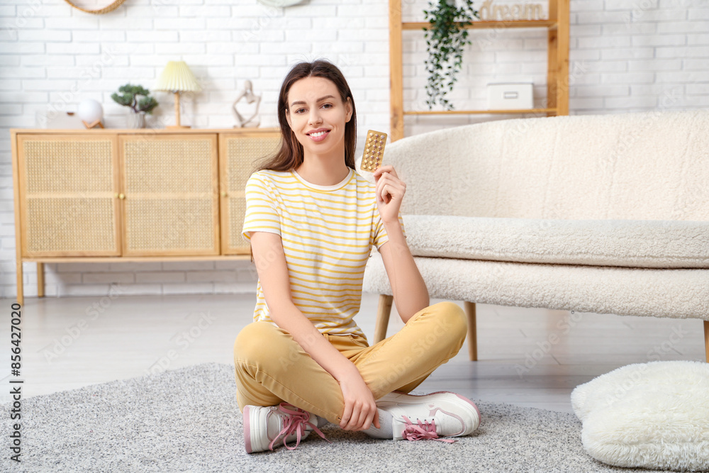 Beautiful young woman with birth control pills sitting on carpet in living room Beautiful young woman with birth control pills sitting on carpet in living room