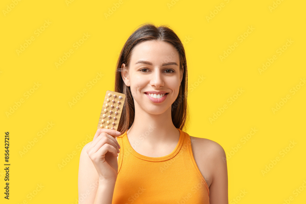 Happy young woman with birth control pills on yellow background Happy young woman with birth control pills on yellow background