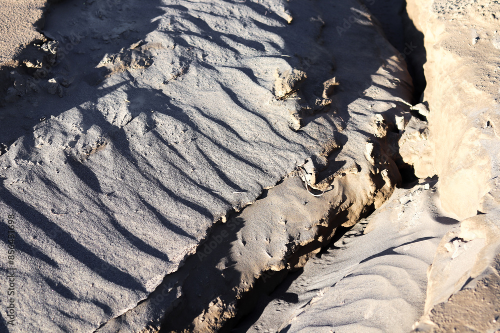 Fototapeta premium Sand texture with deep grooves and shadows. Abstract desert landscape with unique patterns and natural formations.