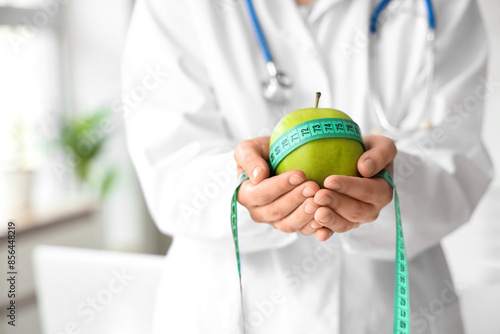 Female nutritionist with apple and tape measure in office, closeup