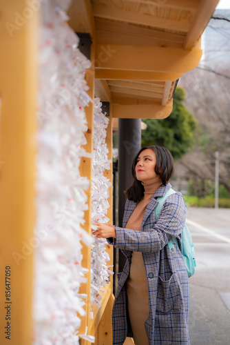 A young Latina woman smiling and making wishes at Zojoji Temple in Tokyo, Japan, tying her hopes to the prayer wall. photo