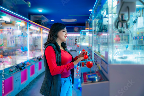 Papier peint Young Latina woman smiling and playing arcade games in Akihabara, Tokyo, Japan, surrounded by colorful lights and machines