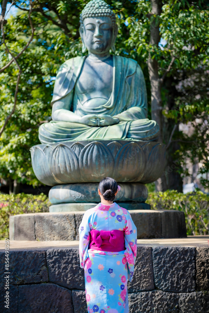 Unrecognizable young Latina woman in a kimono, standing in front of a large Buddha statue in Ueno Park, Tokyo, Japan, enjoying the serene atmosphere. Unrecognizable young Latina woman in a kimono, standing in front of a large Buddha statue in Ueno Park, Tokyo, Japan, enjoying the serene atmosphere.