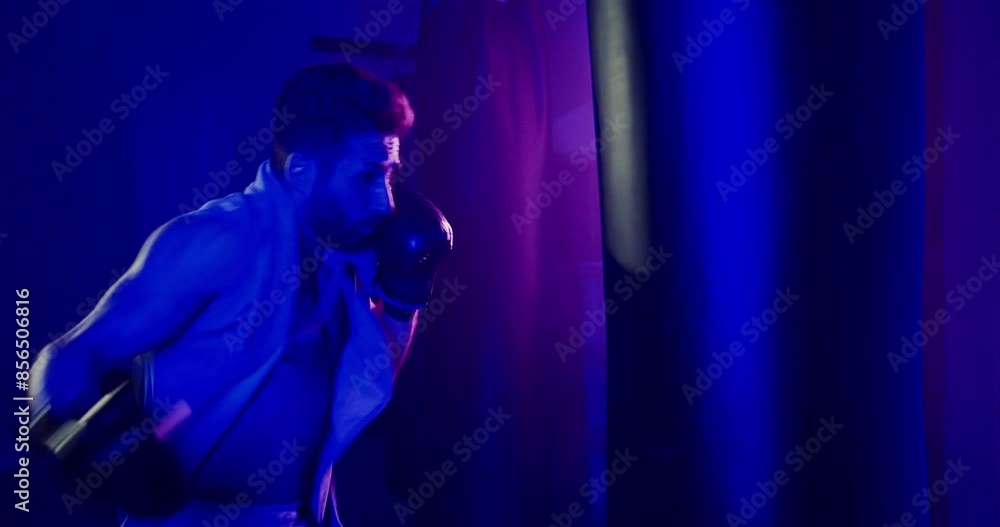 Man Punching Punching Bag in Dark Neon-lit Room Man Punching Punching Bag in Dark Neon-lit Room