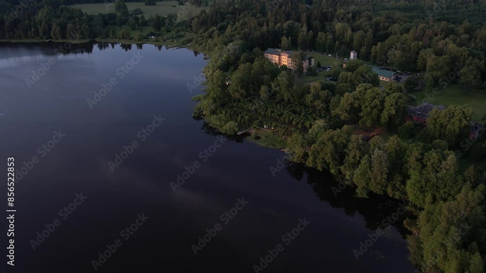 A stunning drone view of Katvari village at sunset, highlighting the Katvari linden tree by the lake. The golden sunlight casts a warm glow over the tranquil water. A stunning drone view of Katvari village at sunset, highlighting the Katvari linden tree by the lake. The golden sunlight casts a warm glow over the tranquil water.