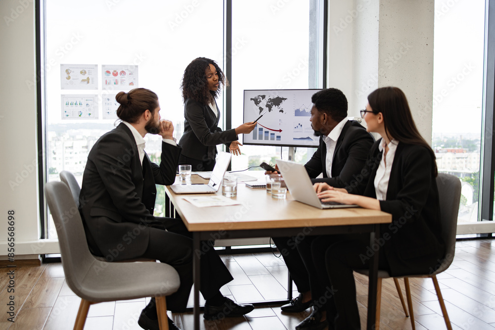 Business professionals discussing company strategy during office meeting. Woman presenting graphs on screen while colleagues listen attentively. Modern office with large windows and city view. Business professionals discussing company strategy during office meeting. Woman presenting graphs on screen while colleagues listen attentively. Modern office with large windows and city view.