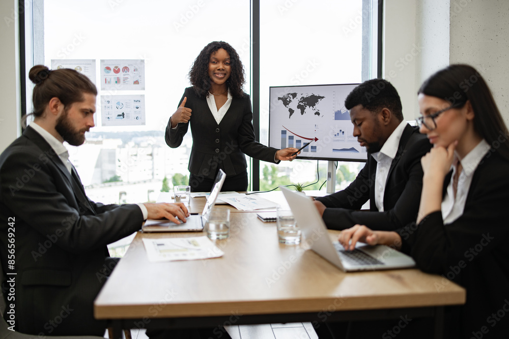 Business meeting with diverse team discussing charts and data analysis. Woman presenting data on screen while colleagues listen and take notes. Professional workspace with city view. Business meeting with diverse team discussing charts and data analysis. Woman presenting data on screen while colleagues listen and take notes. Professional workspace with city view.