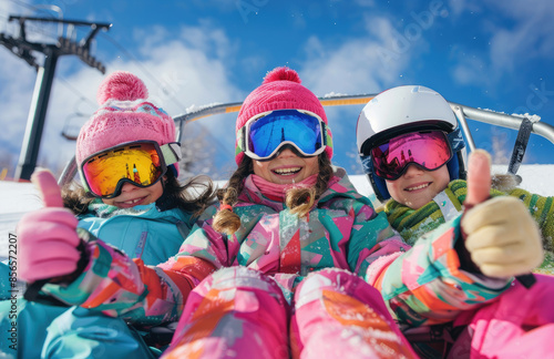 happy young girls in colorful ski , wearing helmets and goggles sitting on the chair at snow hill with blue sky background.