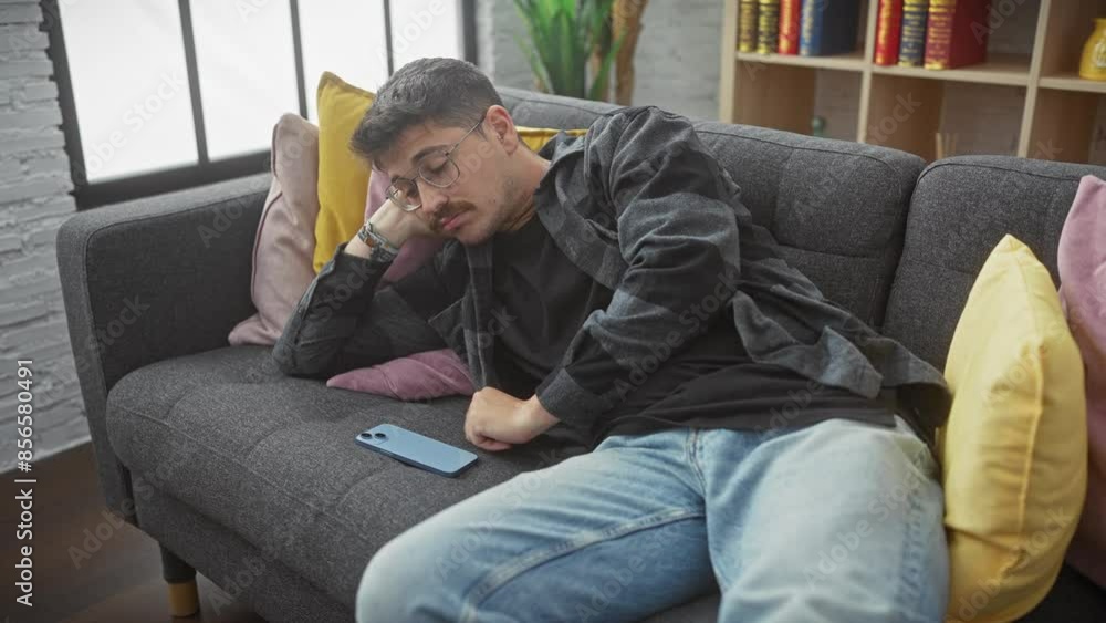 Hispanic man lounging on sofa with phone, apartment living room, casual relaxation, indoor leisure Hispanic man lounging on sofa with phone, apartment living room, casual relaxation, indoor leisure