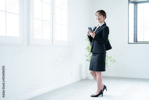 室内で携帯を持つスーツを着た若い日本人女性 photo
