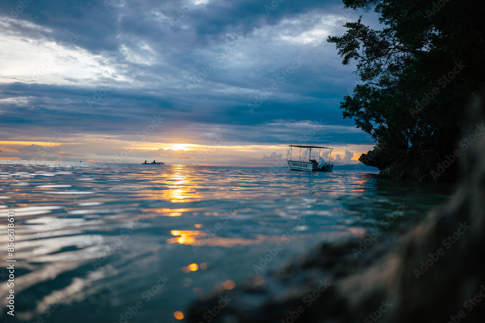 Fototapeta premium Boat floating on calm sea during sunset, reflecting beautiful colors on the water