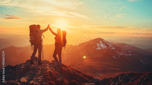 Two hikers high-five on top of the mountain at sun rise, in silhouette.