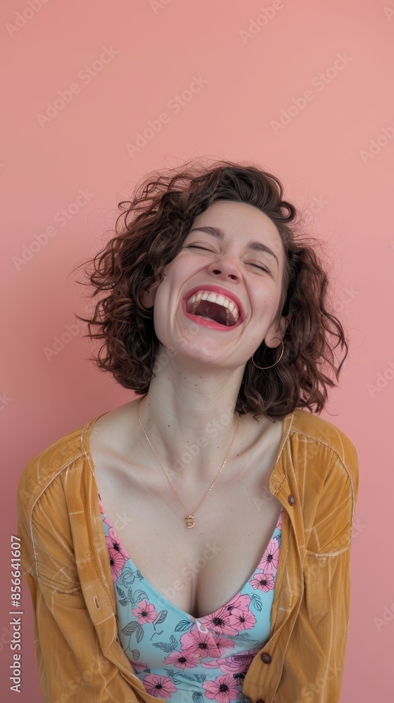 A young woman with curly hair laughs in front of a pink wall A young woman with curly hair laughs in front of a pink wall