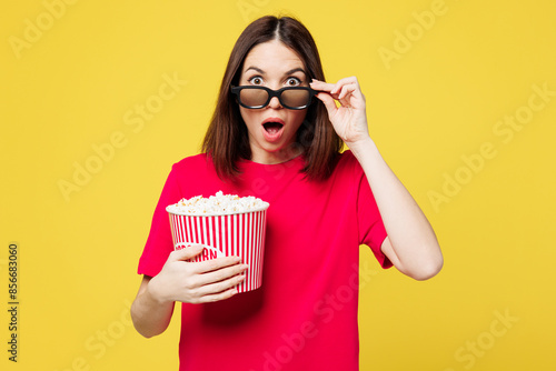 Young sad shocked surprised woman wear pink t-shirt casual clothes lower 3d glasses watch movie film hold bucket of popcorn in cinema look camera isolated on plain yellow background studio portrait.