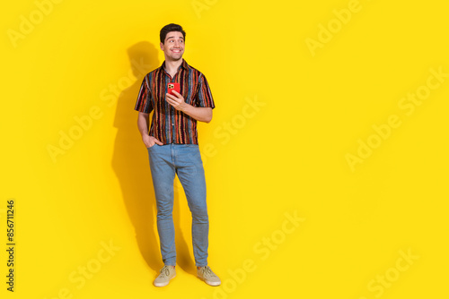 Full size photo of nice young man hold phone look empty space wear shirt isolated on yellow color background