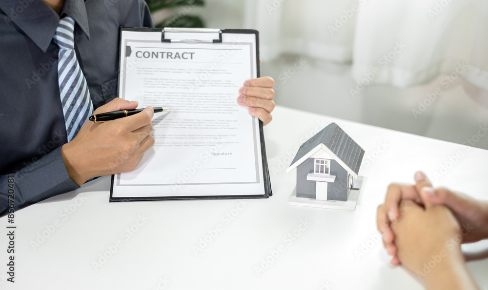A real estate agent with a House model is talking to clients about buying home insurance. Home insurance concept A real estate agent with a House model is talking to clients about buying home insurance. Home insurance concept