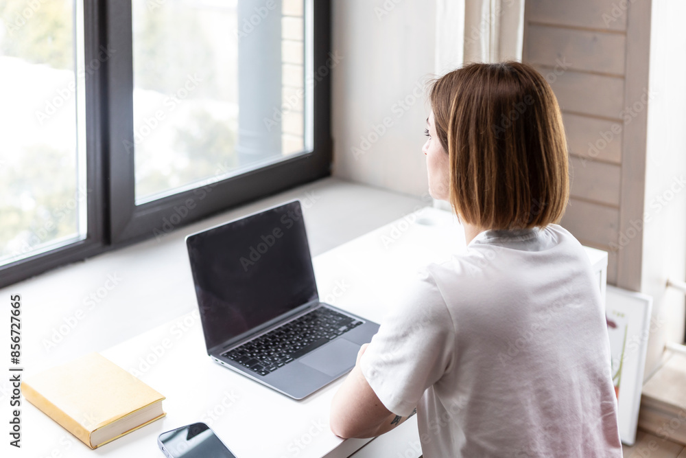 Fototapeta premium Back view on Young female student sitting at the desk at home and preparing for a new academic year. Education and online training concept