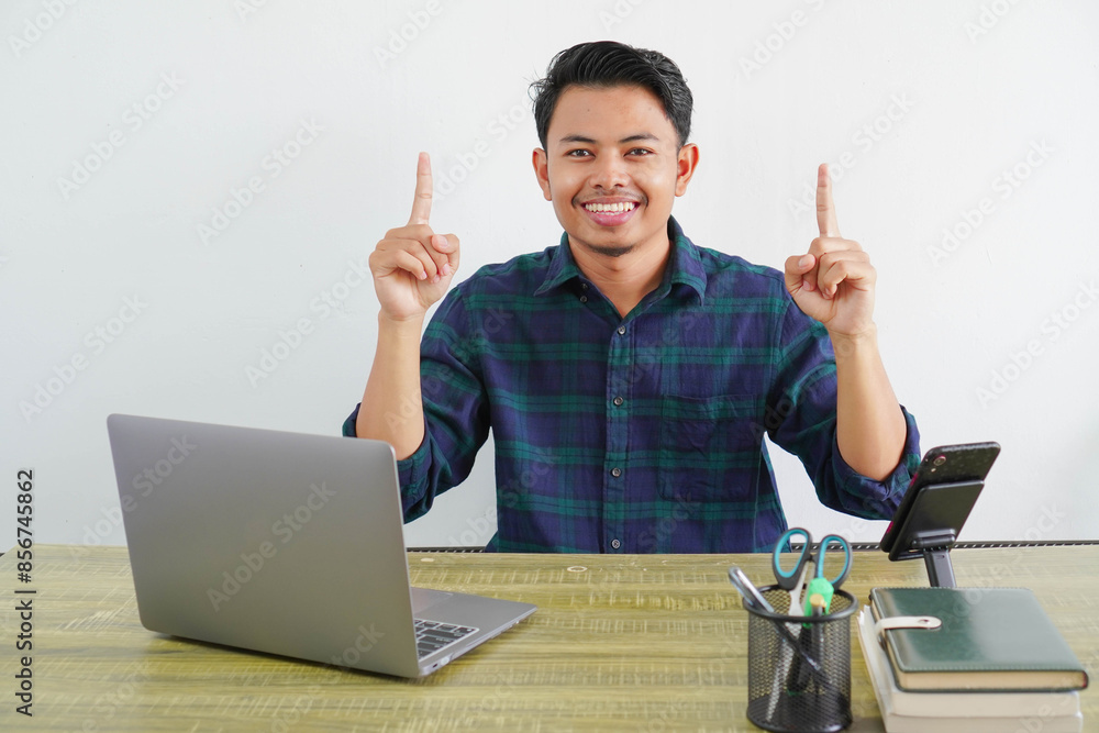 cheerful young asian man sit work at wooden desk with pc laptop. Achievement business career lifestyle concept. pointing index fingers up cheerful young asian man sit work at wooden desk with pc laptop. Achievement business career lifestyle concept. pointing index fingers up