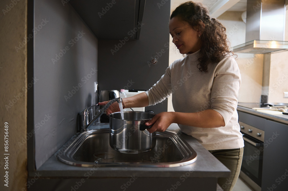 Woman filling pot with water in modern kitchen sink Woman filling pot with water in modern kitchen sink